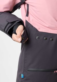 Giacca impermeabile con una parte superiore rosa e una parte inferiore grigia scura. Le caratteristiche includono una chiusura con bottone, polsini regolabili e tasca con zip.