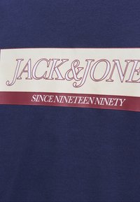 T-shirt bleu marine avec une bande horizontale crème portant le texte rouge "JACK & JONES" et "SINCE NINETEEN NINETY."