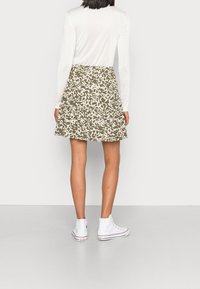 Hame verde con patrón y volantes, hecha de material ligero. Combinada con una blusa blanca de manga larga y zapatillas altas blancas.