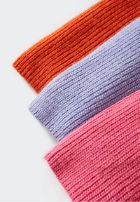 Trois pulls en tricot pliés, de couleurs orange, violet clair et rose, sur un fond blanc.