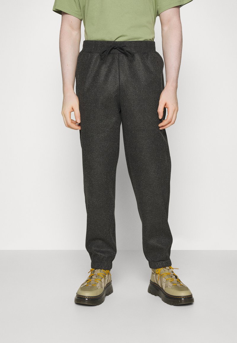 Pantalons de jogging texturés gris foncé avec taille élastique et cordon de serrage. Associés à des chaussures beiges et noires avec des lacets jaunes.