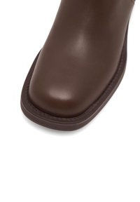 Boots din piele maro până la gleznă, cu vârf pătrat, textură netedă și talpă rezistentă. Prezintă cusături contrastante pe margini.