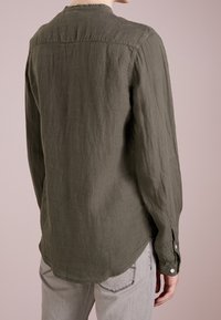 Olivově zelená, dlouhá košile s dlouhým rukávem vyrobená z texturované látky, s kulatým spodním lemem a knoflíkovými manžetami, zobrazená zezadu.