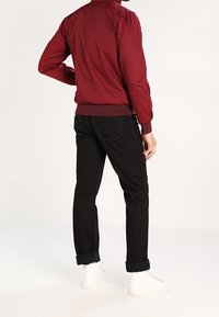 Giacca bomber color granata con polsini e orlo a coste, abbinata a jeans neri con risvolti e sneakers bianche. Design pulito, look casual.