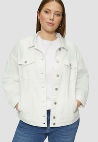 Witte denim jas met een kraag, drukknopen, twee voorzakken en een relaxte pasvorm. Gedragen over een wit T-shirt en blauwe spijkerbroek.