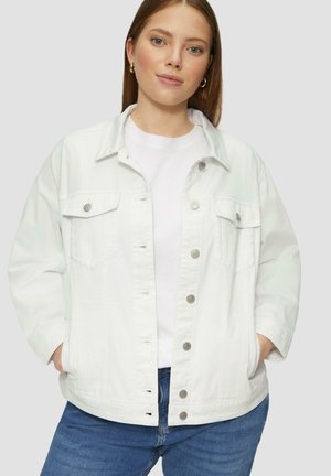 Veste en denim blanche avec un col, des boutons-pression, deux poches avant et une coupe décontractée. Portée par-dessus un t-shirt blanc et un jean bleu.