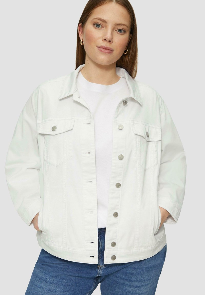 Witte denim jas met een kraag, drukknopen, twee voorzakken en een relaxte pasvorm. Gedragen over een wit T-shirt en blauwe spijkerbroek.