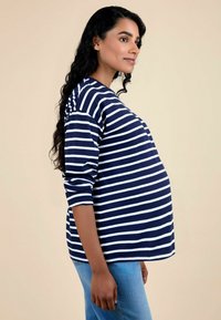 Top de maternidad a rayas en azul marino y blanco con mangas largas, cuello redondo y corte holgado. Combinado con jeans de mezclilla azul claro.