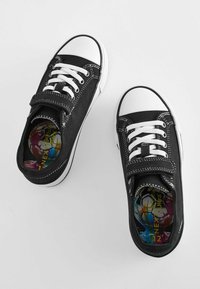 Sorte lærreds sneakers med hvide gummisåler og tåkapper, med hvide snørebånd og en velcrorem. Farverige indlægssåler synlige indeni.