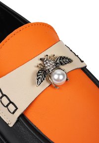 Kolorowe loafersy z pomarańczową skórzaną cholewką, beżowym paskiem i czarną podeszwą. Zawierają akcent w postaci pszczoły ozdobionej kryształami i perłą.