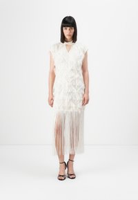 Witte jurk met gelaagde franjeranden, sleutelgate halslijn en midi-lengte. Draag het met zwarte sandalen met spaghettibandjes. Soepele textuur, getailleerde silhouet.