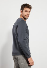 Sudadera gris oscuro de manga larga y cuello redondo. Cuenta con puños y bajo de canalé, y una textura de tela suave.