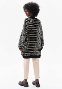 Zwart en crèmekleurig patroon oversized trui met een geometrisch ontwerp, gecombineerd met lichtbeige broeken en zwarte platform schoenen.