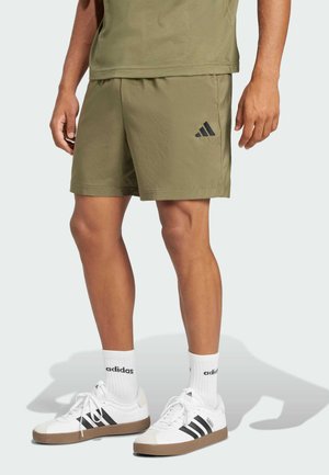 Pantaloni sportivi verdi con logo ricamato nero, abbinati a sneaker bianche con strisce nere e calze bianche. Vestibilità corta e rilassata.