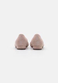 Chaussures en daim rose clair avec un petit talon bloc, un bout arrondi et une texture lisse. La vue de derrière montre un design minimaliste sans ornements.