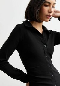 Svart långärmad skjorta med krage, slim fit-design och knappstängning fram. Slät tyg med en subtil lyster och lätt textur.