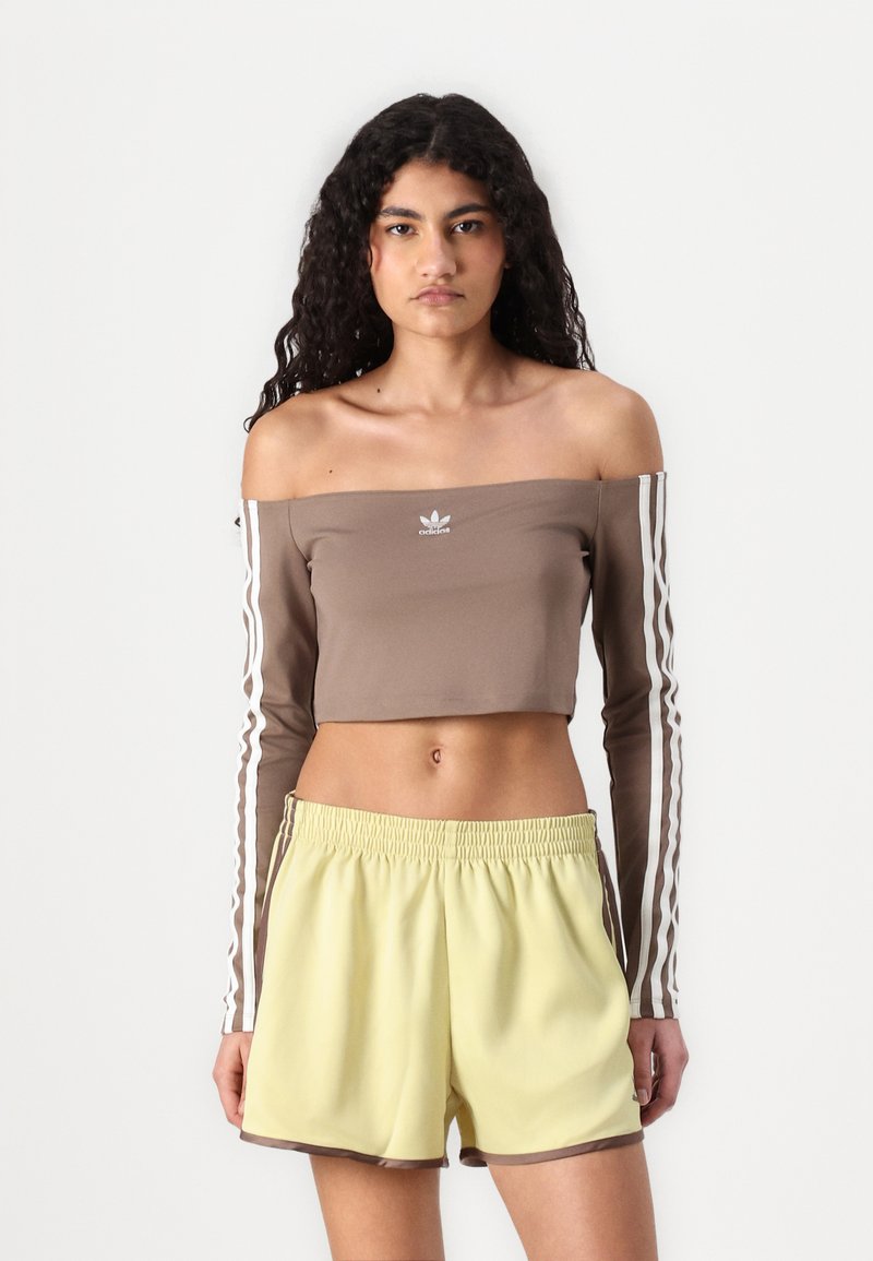 Top cropped castanho com mangas longas, com um design off-the-shoulder e listras brancas. Combinado com calções amarelos claros com um cós elástico.