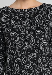 Top in tessuto nero con una stampa paisley e floreale bianca. Collo rotondo e maniche lunghe con texture morbida.