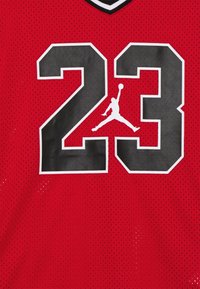 Červený síťovaný basketbalový dres s černými čísly "23" s bílým obrysem a logem Jumpman, s designem do V a prodyšnou texturou.