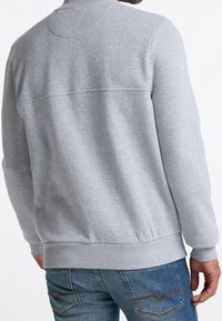 Grauer Hoodie mit Rundhalsausschnitt, gerippten Bündchen und Saum, flachen Nähten sowie einem mittelschweren, weichen Stoff, kombiniert mit blauen Jeans.