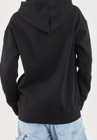 Sweat à capuche noir, avec une texture douce, des manches longues et une coupe décontractée. Coutures visibles à l'ourlet, porté avec un pantalon cargo bleu clair.