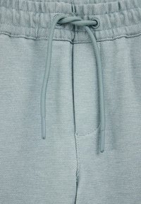 Heledsinised spordipüksid, mis on valmistatud tekstureeritud kangast. Need on varustatud elastse vöökoha ja reguleeritava paelaga ning neil on minimaalsed õmblusdetailid.