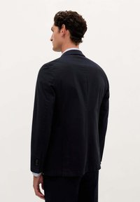 Blazer navy con un ajuste entallado, hombros estructurados y una única abertura. Presenta puños con botones y una suave tela de algodón.