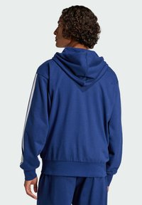 Blue hooded sweatshirt made of cotton blend. Features ribbed cuffs and hem, with contrasting white stripes along the sleeves. Smooth texture.