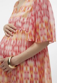 Prozorna, lepršava obleka s pink in oranžno vzorcem. Ima kratke lepršave rokave in ohlapen kroj, nosi se z zlatim zapestnico na zapestju.