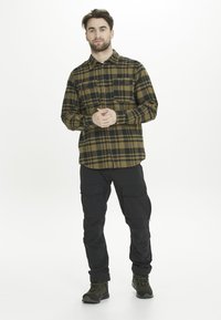 Bruin en zwart geruit flanellen shirt met knoopsluiting en borstzakken, gecombineerd met zwarte cargo pants en olijfgroene wandelschoenen.
