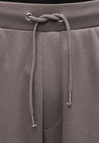 Ανοιχτό γκρι παντελόνι τζόγκερ με ριμπ ζώνη μέσης, ρυθμιζόμενο κορδόνι με μεταλλικά άκρα και πλαϊνή τσέπη, κατασκευασμένο από απαλό υφασμένο ύφασμα.