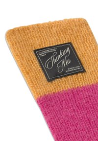 Strikket stof i orange og pink med en sort etiket, der står "Thinking Mu" og "Et moderne middelhavstvist."