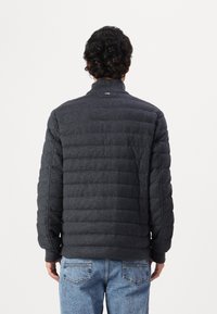 Veste rembourrée gris foncé avec un col haut. Dotée d'un motif matelassé horizontal et de poignets côtelés, assortie à un jean en denim bleu clair.