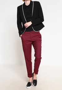 Svart kavaj med vit piping, i kombination med vinröda mönstrade byxor och svarta slip-on skor. Slät tygkvalitet med skräddarsydd passform.