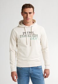 Cremefarbener Kapuzenpullover aus weichem Stoff; mit einer Kängurutasche, Kordelzügen am Hals und einem grafischen Druck auf der Vorderseite.