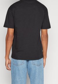 Černé bavlněné tričko s kulatým výstřihem a krátkými rukávy. Na zadní straně má rovný lem a ploché švy. V kombinaci s světle modrými džínami.