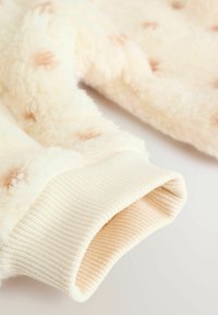 Fleece-pull i cream med ljusbruna accenter, med en mjuk textur och ribbad mudd. Designen har fläckar för extra detalj.