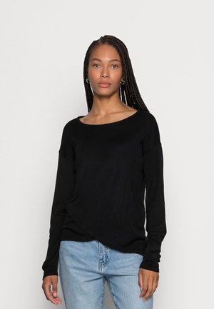 Black long-sleeve top with a wide neckline, soft texture, and draped design, paired with light blue denim jeans.