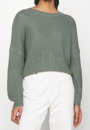 Maglione verde a maglia con una vestibilità ampia, polsini larghi e scollatura a barca, abbinato a pantaloni bianchi a vita alta. Design testurizzato e a coste.
