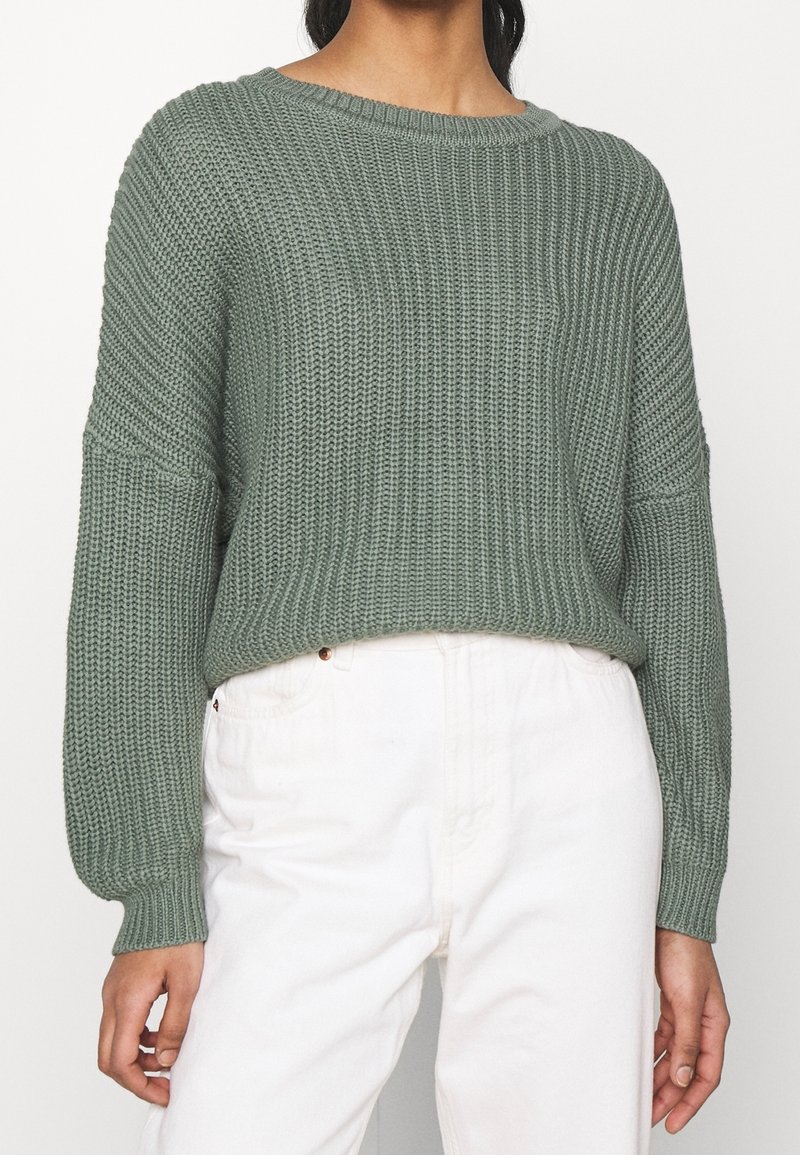 Maglione verde a maglia con una vestibilità ampia, polsini larghi e scollatura a barca, abbinato a pantaloni bianchi a vita alta. Design testurizzato e a coste.