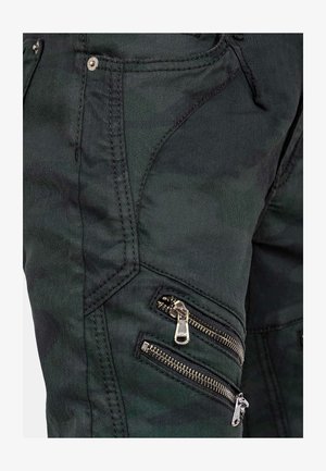 Zwarte camouflage cargobroek heeft een aansluitend ontwerp met meerdere ritszakken. Het materiaal is duurzaam, met zichtbare stiksels en ritsen.