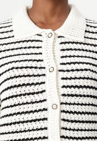Strikket cardigan med svart-hvite striper. Har krage og sentral knappelukking.