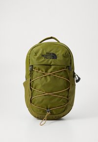 Olive žalia spalvos "North Face Borealis Mini" kuprinė su priekyje esančia elastinga virve, viršutine rankena ir šoninėmis kišenėmis, pateikta prieš baltą foną.