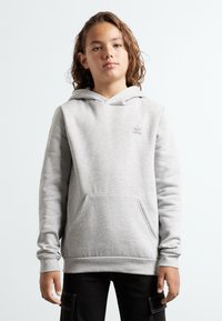 Grå huvtröja med en framficka, ribbade ärmslut och nederkant. Har en liten lila adidas-logotyp på bröstet. Tyget verkar mjukt.