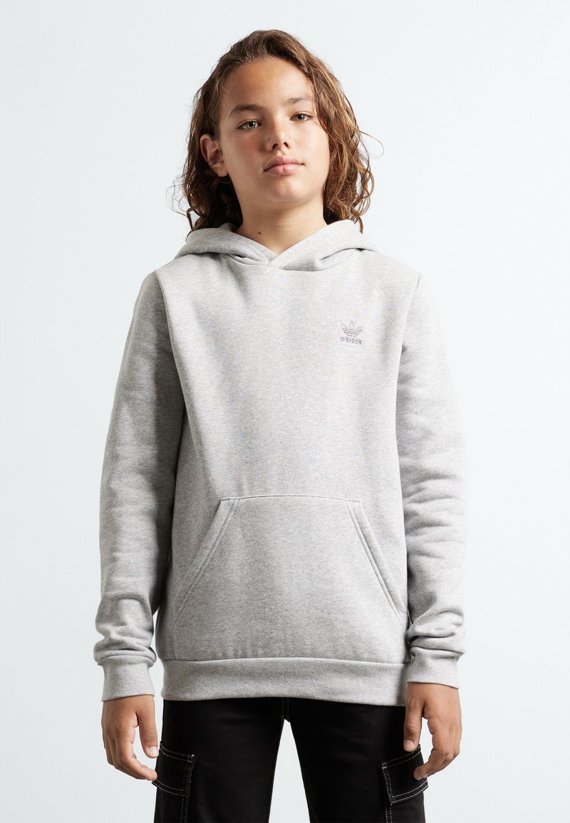 Grå huvtröja med en framficka, ribbade ärmslut och nederkant. Har en liten lila adidas-logotyp på bröstet. Tyget verkar mjukt.