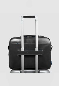 Bolsa para portátil de cuero negro con un robusto asa de trolley de aluminio gris, que cuenta con un compartimento principal con cremallera y un bolsillo lateral con detalles en azul.