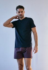 Granatowa koszulka z krótkim rękawem w połączeniu z szortami w czerwono-niebieską kratkę. Materiał wydaje się miękki, a krój jest luźny, z minimalnymi detalami designu.