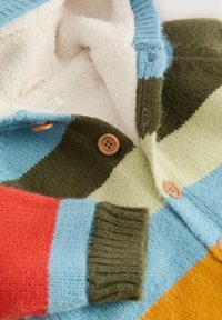 Sweter z dzianiny o paskowanym wzorze w kolorze niebieskim, zielonym, czerwonym i pomarańczowym, z miękkim beżowym podbiciem z polaru oraz drewnianymi guzikami.