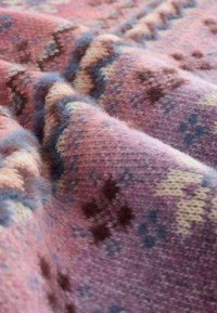 Villa vilt med en teksturert rosa base og geometriske mønstre i brunt og blått, som viser intrikat strikkedetaljering og myke fibre.