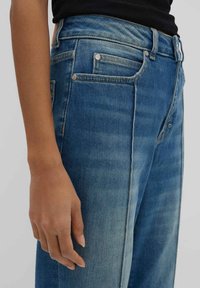 Jeans in denim blu con vita alta, caratterizzati da un lavaggio sbiadito, design classico a cinque tasche, bottoni metallici e una texture liscia.